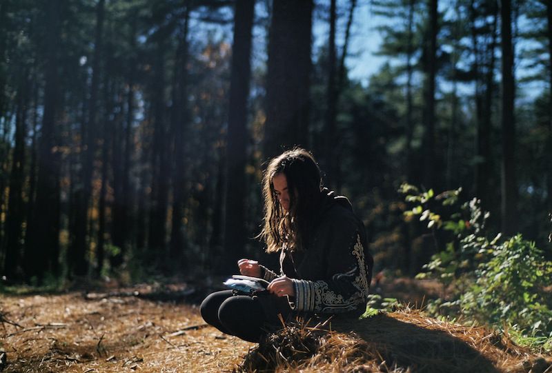 Una chica sentada en el bosque leyendo.